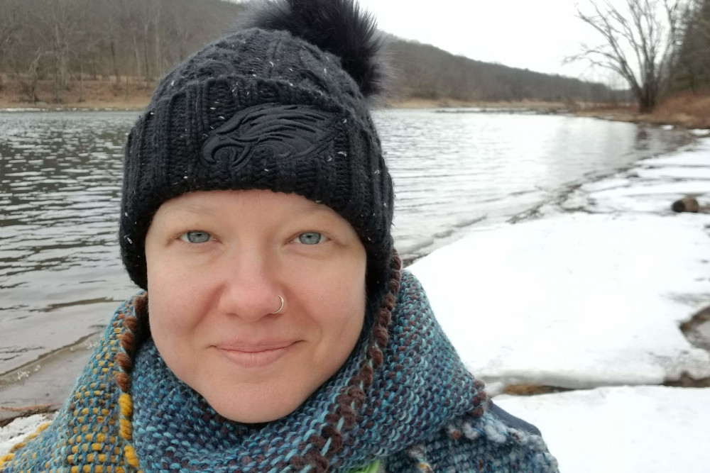 close up photo of a woman in a winter hat standing by a snowy Delaware River