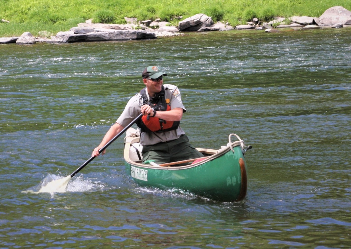 Photo of a uniformed park ranger smiling and paddling a green canoe in a river