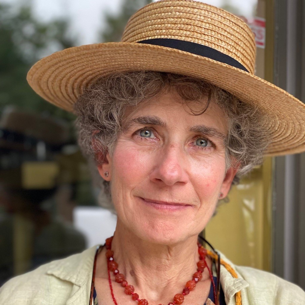 A photo of Rebekah Creshkoff, a woman with short curly hair and a straw hat