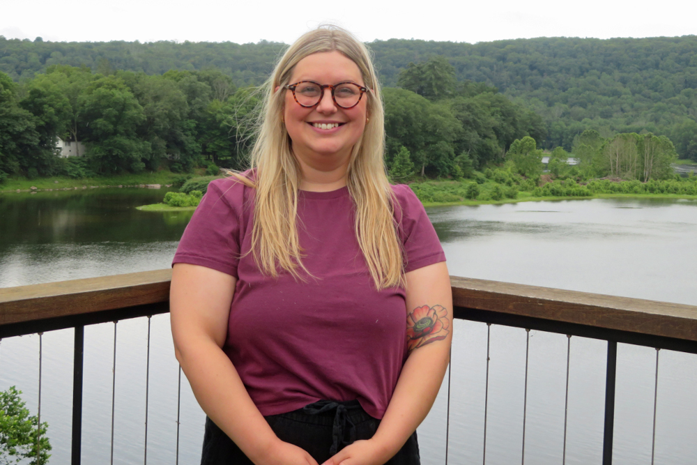 picture of a blonde woman with glasses standing on a balcony overlooking the Delaware River